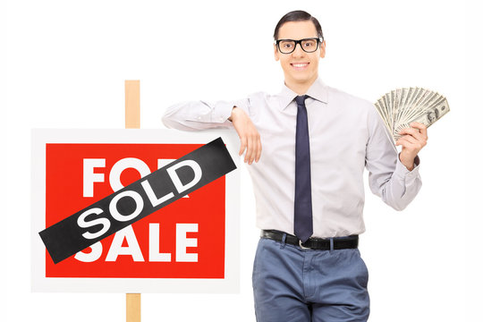 Male realtor holding money next to a sold sign