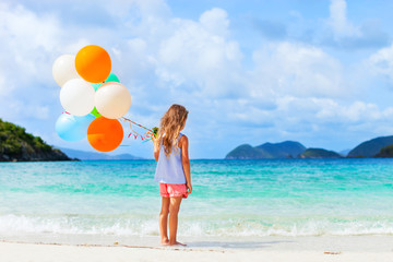 Back view of little girl with balloons at beach