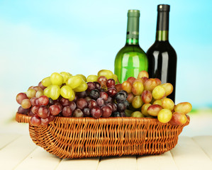 Ripe grapes in wicker basket, wine bottles, on bright