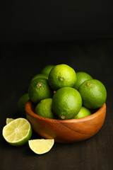 Fresh juicy limes in wooden bowl, on dark background