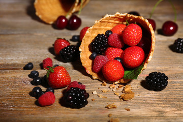 Different ripe berries in sugar cone, on wooden background