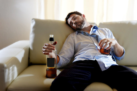 drunk businessman sleeping in couch whiskey bottle wasted