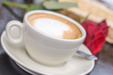 Blurred white cup of coffee with rose