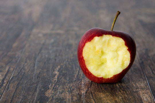 Red apple with a hole bitten into it on a brown surface