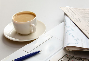 Cup of coffee near the laptop and newspapers