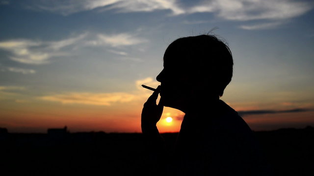 Silhouette of young adult woman smoking a cigarette in sunset