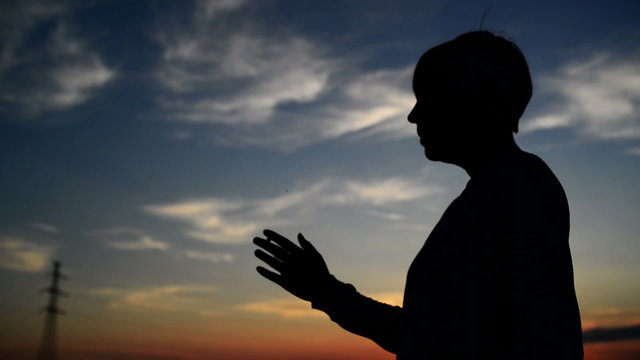 Silhouette of young adult woman smoking a cigarette in sunset.