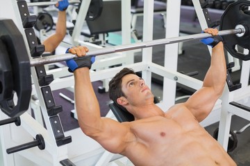 Shirtless muscular man lifting barbell in gym