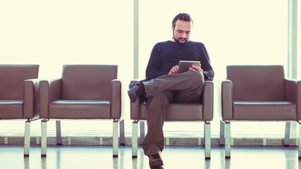 Man using digital tablet pc at an airport lounge, waiting room. © andreaobzerova