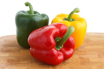 Red, yellow, green peppers on chopping board, white background.