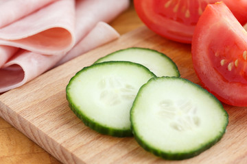 Sliced cucumber on chopping board with ham and tomato.