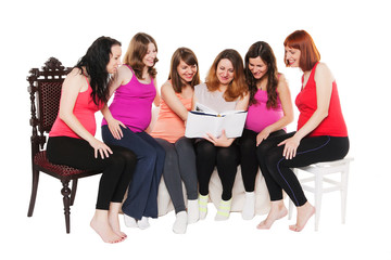six smiling pregnant women sitting and reading a book