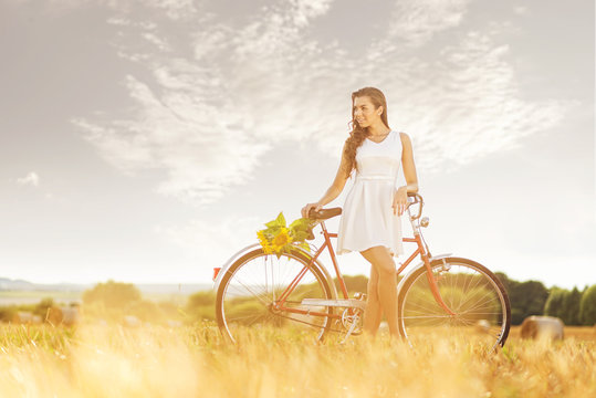 Beautiful woman old bicycle with flowers in wheat field