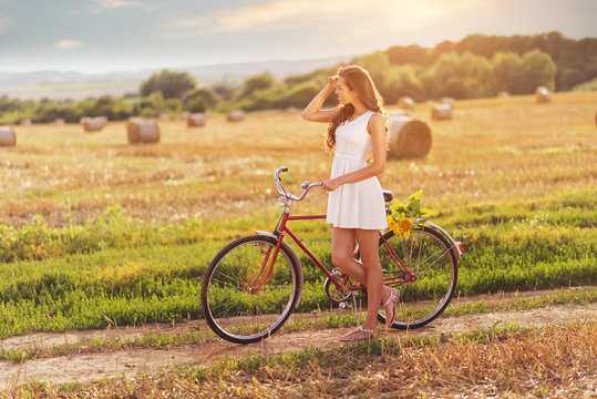 Beautiful woman old bicycle with flowers in wheat field 
