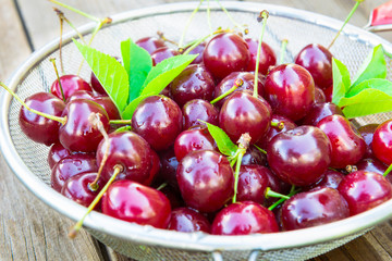 Fresh cherry in colander on wooden table