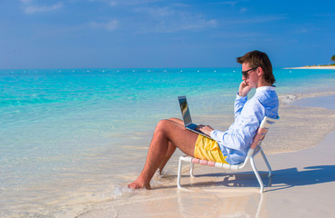 Young businessman using laptop on tropical beach