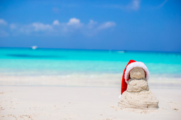 Fototapeta na wymiar Little sandy snowman with red Santa Hat on white Caribbean beach