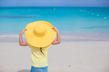 Fototapeta na wymiar Little girl in a big yellow straw hat on white sand beach
