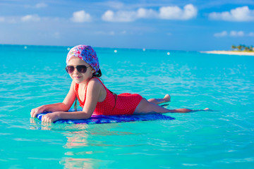 Little cute girl swimming on a surfboard in the turquoise sea