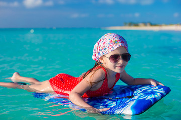 Little adorable girl on a surfboard in the turquoise sea