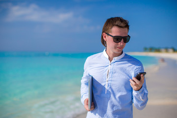 Young businessman using laptop and telephone on tropical beach