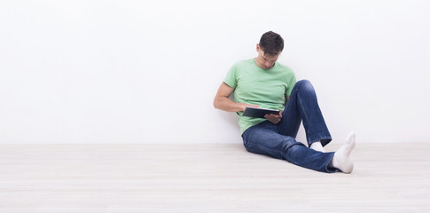 Fototapeta premium man using a tablet pc sitting in front of white wall.