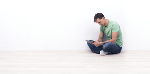 Tablet pc user with copy space sitting against a white wall