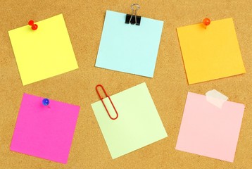 Sticky notes of various colors and fasteners on a bulletin board