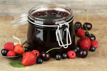 Tasty jam with berries in glass jar on wooden table