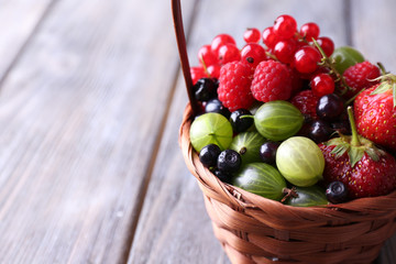 Forest berries in wicker basket, on wooden background