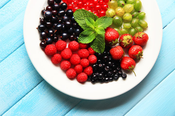 Forest berries on plate, on color wooden background