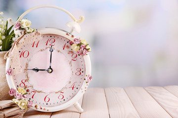 Beautiful vintage alarm clock with flowers on light background