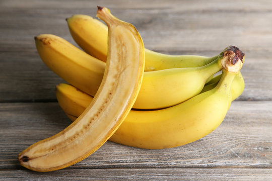 Halved and whole ripe bananas on wooden background