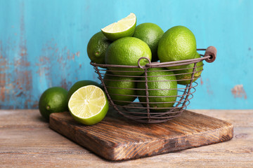 Fresh juicy limes in basket on blue wooden background