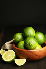 Fresh juicy limes in wooden bowl, on dark background