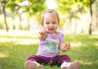 Happy 1 year baby girl holding a flower while sitting on grass in a park. Shallow depth of field