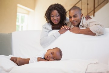 Baby boy sleeping peacefully on couch watched by parents