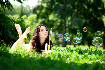 Woman and soap bubbles in park. Beautiful young girl lying on th