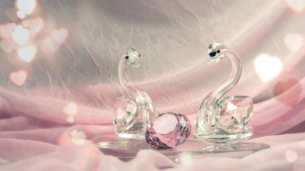 Crystal or glass swans with a diamond on pink cloth