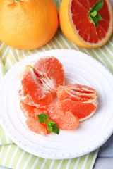 Ripe peeled grapefruits on plate, on color wooden background