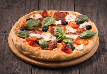 Pizza with salami, mozzarella, olives and basil on rustic wooden