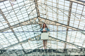 woman with white paper bag standing at mall with glass ceiling