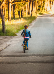brunette girl riding bicycle on road at forest at sunset