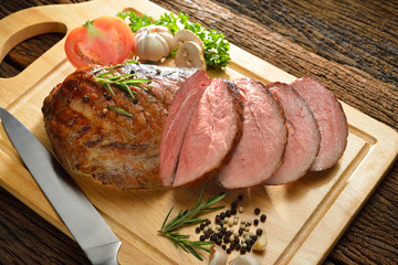 Sliced grilled meat with vegetables on wooden background
