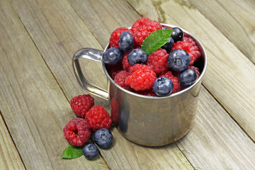 berries and strawberries in a metal cup on wooden background