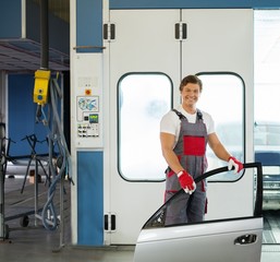 Cheerful serviceman with car door near paint booth