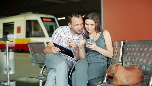 Couple with tablet and smartphone sitting at train station