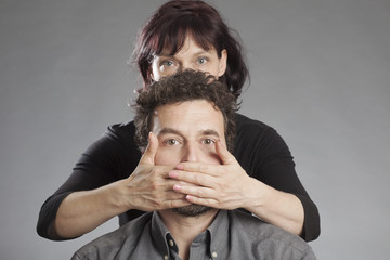 Frau hält Mann den Mund zu.