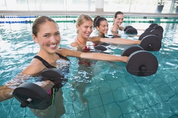 Smiling female fitness class doing aqua aerobics with foam dumbb
