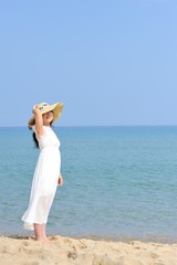 Fototapeta na wymiar 麦わら帽子と白いワンピースを着た女性と夏の海